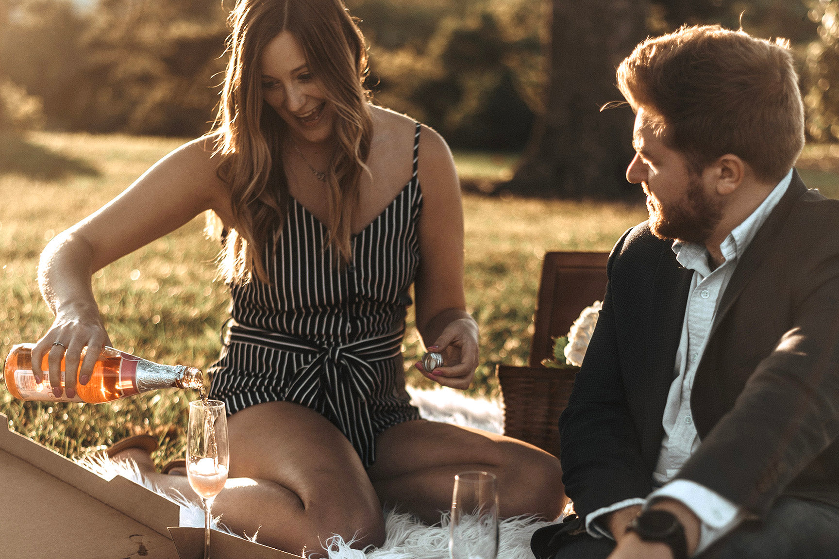 Young couple enjoying a date night drinking champagne and eating pizza at a picnic in the park