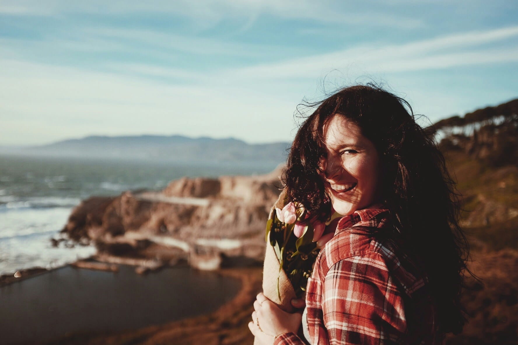 woman overlooking ocean holding pink flowers