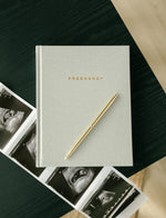Load image into Gallery viewer, Pregnancy Journal with gold pen and sonogram photos on black coffee table