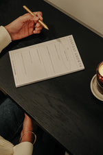 Load image into Gallery viewer, Woman holding a gold pen over the Everyday Growth Notepad on a dark desk with a candle in the background
