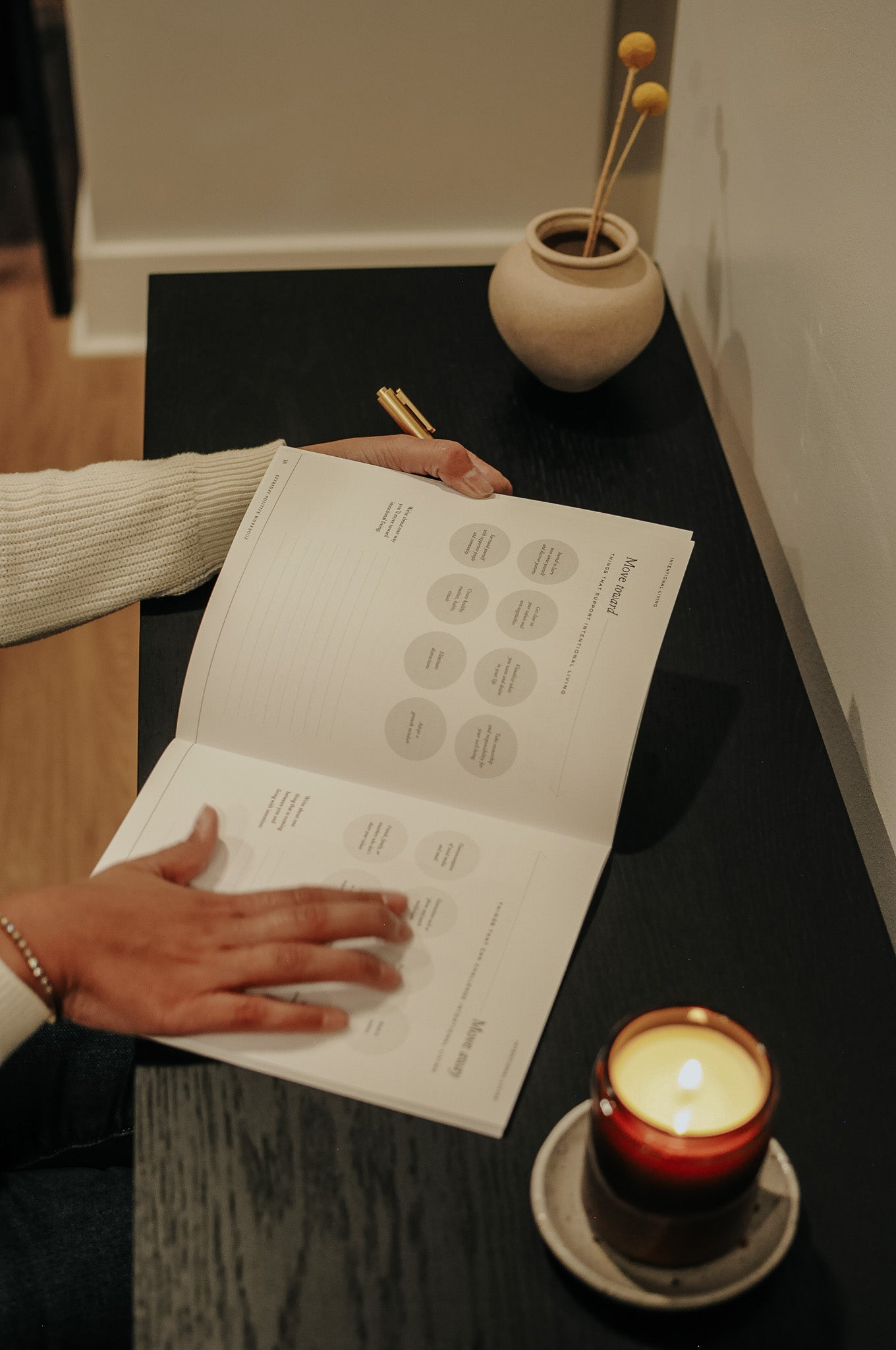 Woman opening Everyday Positive Workbook on desk with candle