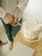 Load image into Gallery viewer, Two people cutting an anniversary cake with the Marriage Journal in the background

